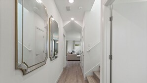 Un pasillo con piso de madera, paredes blancas y una escalera que conduce a un nivel superior.