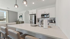 Una cocina moderna con armarios blancos, electrodomésticos de acero inoxidable y una isla central con taburetes de bar.