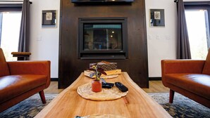 Una sala de estar con una mesa de centro de madera, dos sofás de cuero, un televisor de pantalla plana montado en la pared y cuadros enmarcados en las paredes.