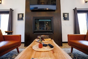 Una sala de estar con una mesa de centro de madera, dos sofás de cuero, un televisor de pantalla plana montado en la pared y cuadros enmarcados en las paredes.