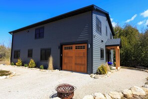 Et moderne hus med to etager, mørk facade, en garageport i træ og en grusvej.