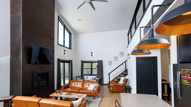 Una sala de estar moderna con un sofá, una mesa de centro y una chimenea. Se ve una escalera que sube a un nivel superior.