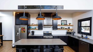 Una cocina moderna con una isla central, taburetes de bar, iluminación colgante, refrigerador, microondas, estufa y una ventana con vistas.