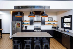 Una cocina moderna con una isla central, taburetes de bar, iluminación colgante, refrigerador, microondas, estufa y una ventana con vistas.