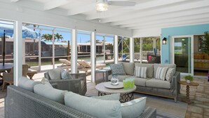 A covered outdoor seating area with wicker furniture, a round table, and a view of the pool and palm trees.