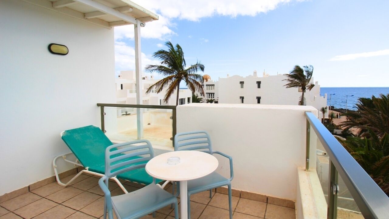 A balcony with a table and chairs, overlooking a beach and palm trees.