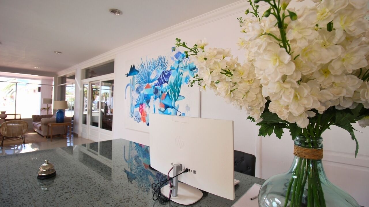 Een moderne hotel lobby met een groot abstract schilderij, een glazen vaas met witte bloemen en een receptiebalie.