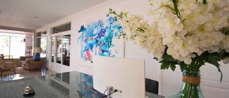 Een moderne hotel lobby met een groot abstract schilderij, een glazen vaas met witte bloemen en een receptiebalie.
