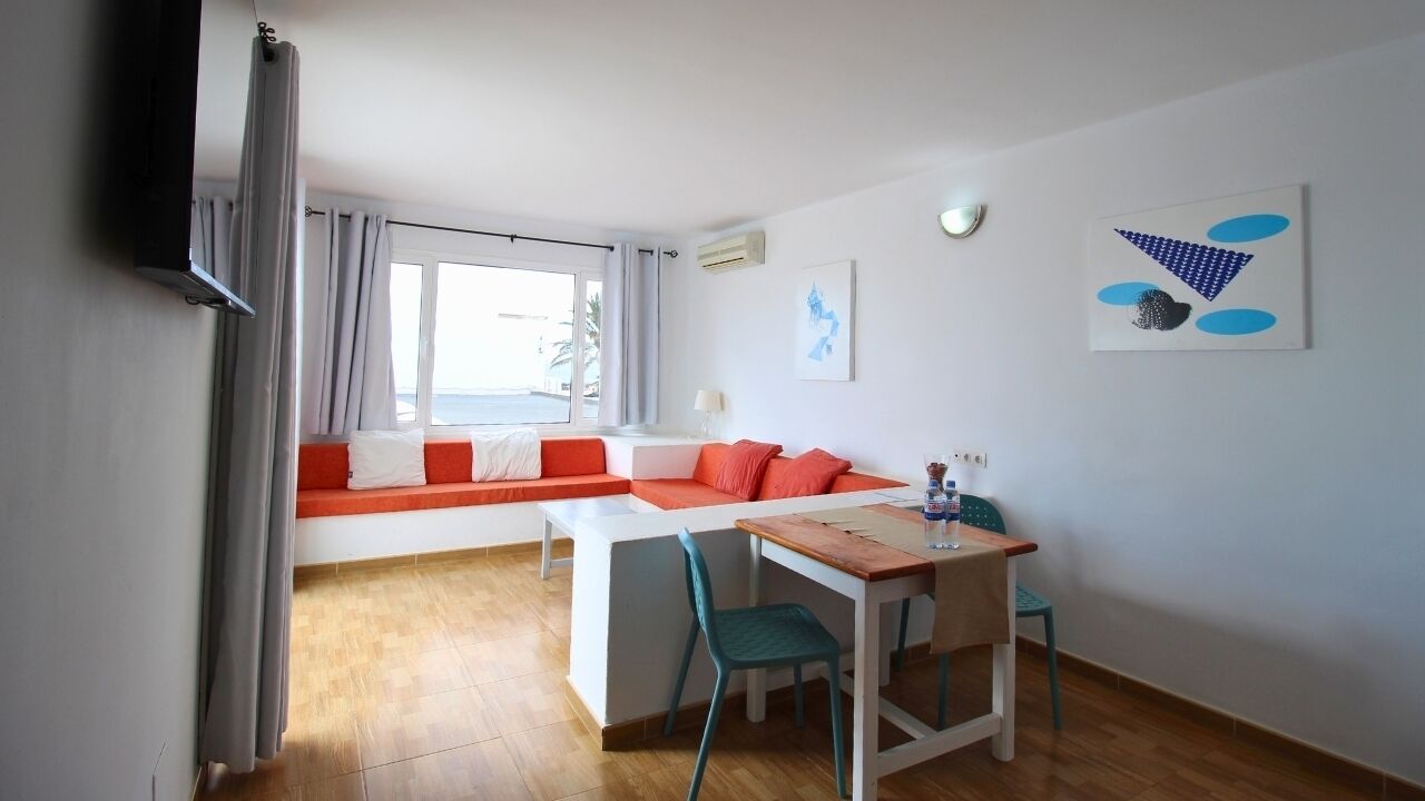 A modern room with a sofa, a dining table, and chairs. There is a window with curtains, a flat-screen TV mounted on the wall, and artwork on the walls.