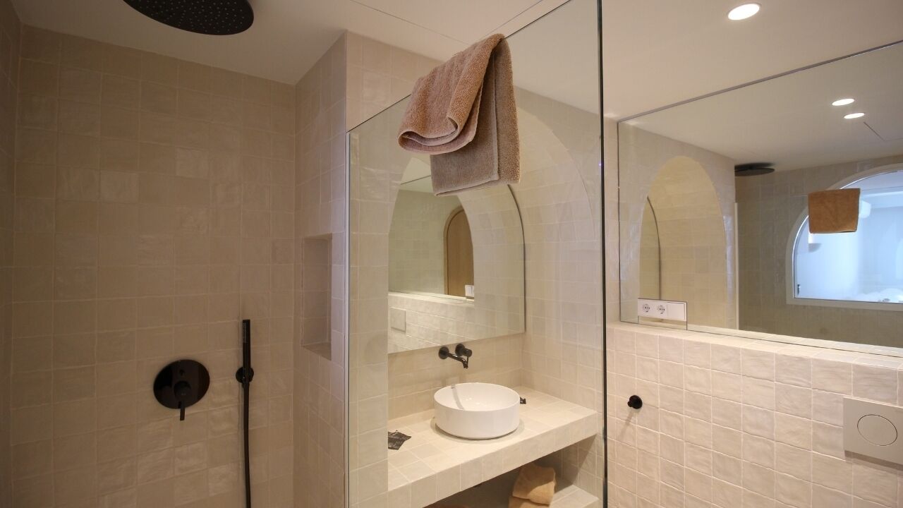 A modern bathroom with a glass-enclosed shower, a round sink, and a large mirror.
