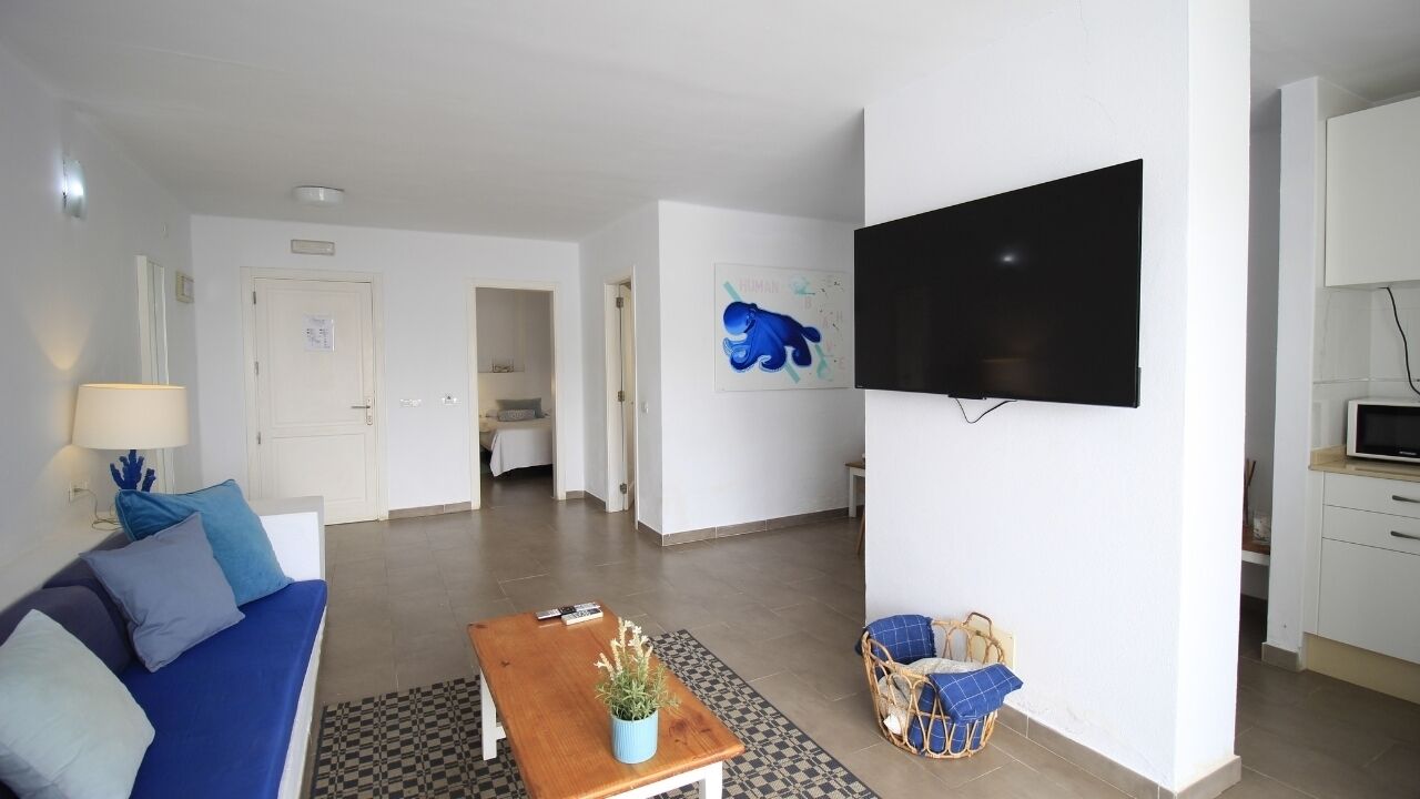 Una sala de estar moderna con sofá, una mesa de centro, televisor y una zona de cocina.