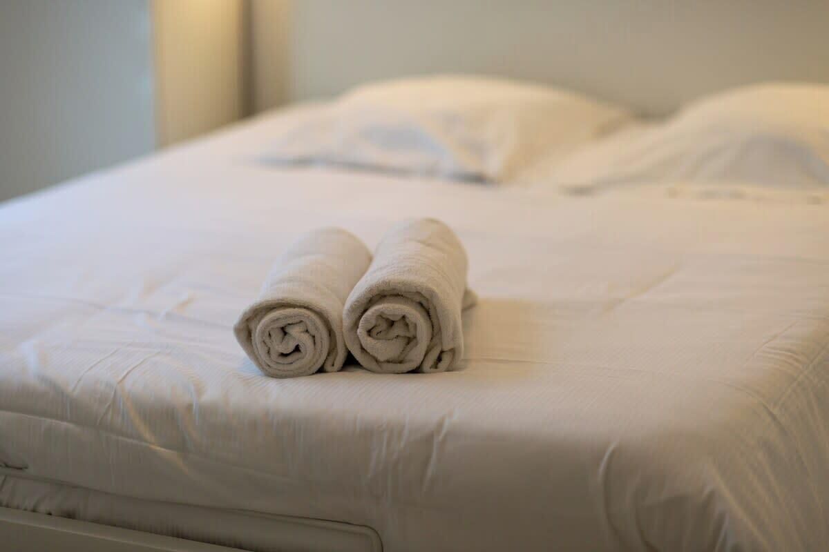 A neatly made bed with two rolled towels placed on the bed.