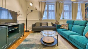 Una sala de estar con un sofá, una televisión, una mesita de centro y una lámpara de pie.