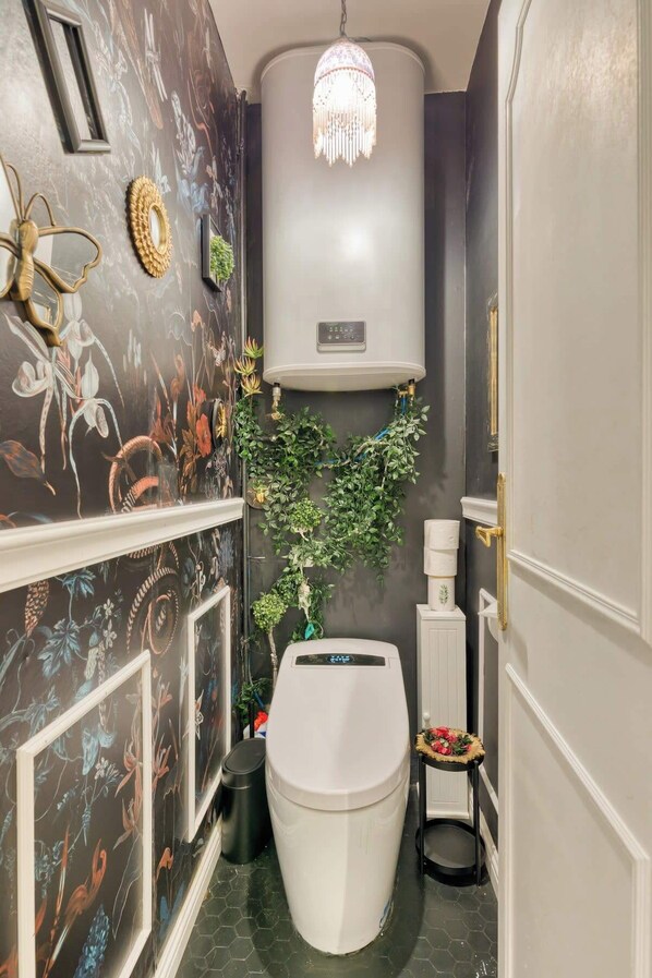 A compact bathroom with a toilet, a wall-mounted heater, and a decorative mirror.