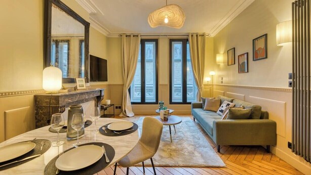 A well-lit living room with a sofa, a dining table set for two, and a large window with curtains. - Olivier : Élégance au Cœur de Rouen (Rouen)