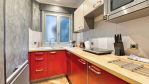 A modern kitchen with red cabinets, a stainless steel microwave, and a window with frosted glass. - Olivier : Élégance au Cœur de Rouen (Rouen)