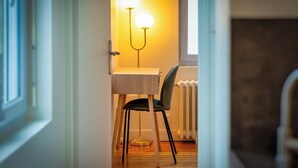 Un estrecho pasillo con suelo de madera, una pequeña mesa con una silla y una lámpara fijada a la pared.