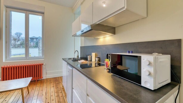 Una cocina moderna con microondas incorporado, ventana con vistas a una casa y suelo de madera.