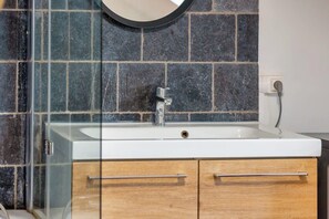 Un baño con cabina de ducha de vidrio, un lavabo blanco y armarios de madera.