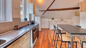 Une cuisine moderne avec un plancher en bois, un coin repas avec une longue table et des chaises, et un petit îlot central doté d’un évier.