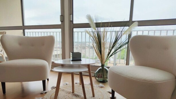 Ein modernes Wohnzimmer mit zwei beigen Sesseln, einem runden Holztisch und einem dekorativen Teppich.