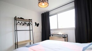 Ein Schlafzimmer mit Bett, Kleiderschrank, Heizkörper, Fenster mit Vorhängen und einem Nachttisch mit Lampe.