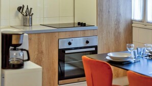 A modern kitchen with a built-in oven, a coffee machine, and a dining area with orange chairs and a table set for two. - Damien, votre *F3 *2 chambres *terrasse à *Rouen (Rouen)