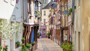 A narrow cobblestone street lined with traditional European buildings, some with balconies and flower boxes.