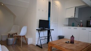 A compact living space with a wooden floor, a bed, a TV on a stand, a dining table, and a kitchenette with cabinets. - Le Petit Nid * en plein centre-ville de Rouen ! (Rouen)