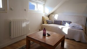A cozy loft bedroom with a sloped ceiling, a wooden table, a radiator, and a bed with patterned pillows. - Le Petit Nid * en plein centre-ville de Rouen ! (Rouen)
