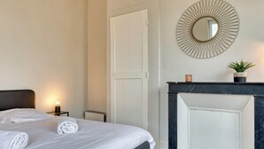 Habitación de hotel con una cama grande, un espejo redondo, una pequeña planta en maceta y una chimenea.