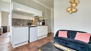 Una cocina moderna con armarios blancos y encimera negra, un sofá azul oscuro con cojines rosados y una mesa de centro con un libro.