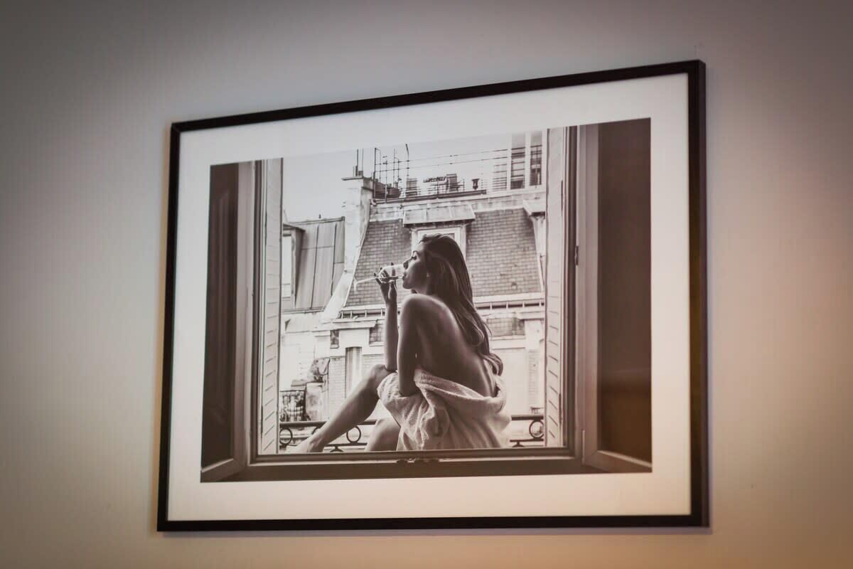 A framed photograph of a person sitting by a window with a cityscape view.