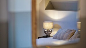 Een hotelkamer met een bed, nachtkastje, lamp en een spiegel die het interieur van de kamer weerkaatst.