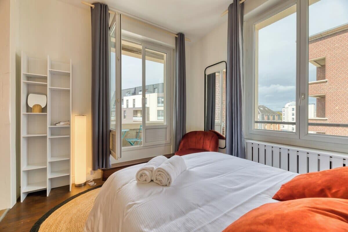 Une chambre d’hôtel équipée d’un lit, d’une chaise, d’une armoire et de grandes fenêtres donnant sur des immeubles.