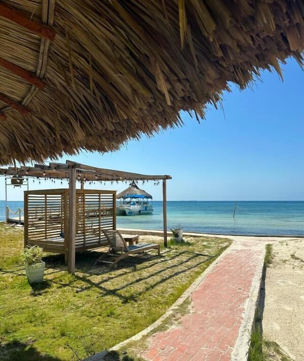 A beachside gazebo with a thatched roof, a wooden bench, and a potted plant. - Quinta del Mar Crystal Beach (Isla Tintipan)