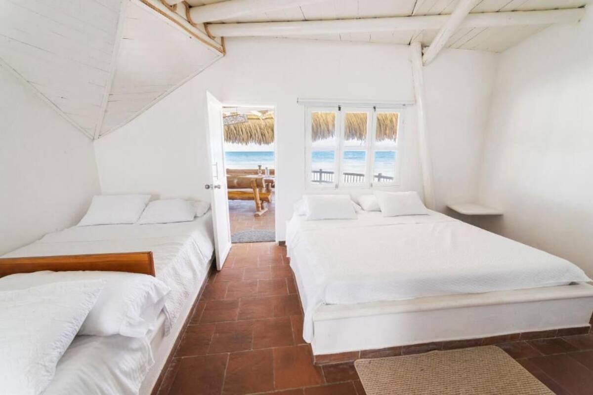 A room with two beds, a view of the beach, and a thatched roof outside.