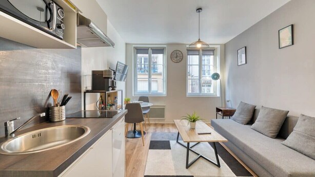 Una cocina moderna con horno empotrado, un comedor con mesa y sillas, un sofá y un ventanal que proporciona luz natural.