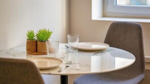 Una mesa de comedor redonda con cubierta de mármol blanco, dos cestas tejidas con plantas verdes y dos vasos de vidrio transparente.