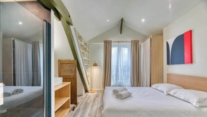 Een moderne hotelkamer met een houten bed, een glazen douchecabine, een houten trap en een groot raam met gordijnen.