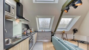Een functionele keuken met een inbouwmagnetron, een spoelbak en een zithoek met een blauwe bank en een klein tafeltje.
