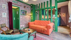 En hyggelig stue med en murstensvæg, grønne detaljer, en lys orange sofa og en vintage lænestol.