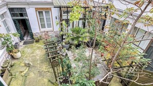 En gårdhave med krukker, planter, et træhegn og en bygningseingang.