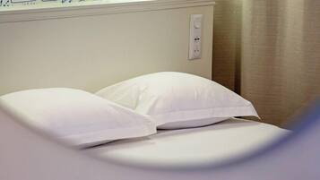 A bed with white bedding in a room with a white wall and a power outlet.