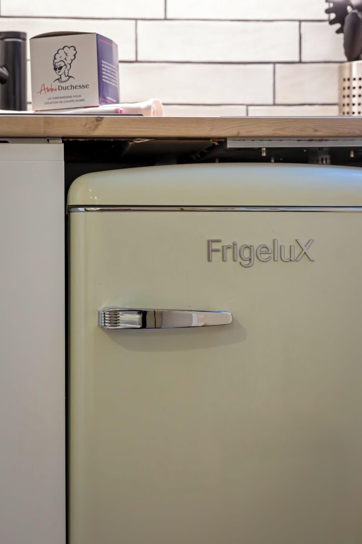 A vintage FrigeluX refrigerator in a kitchen with a tiled backsplash and a wooden countertop.