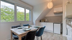 A modern kitchen with a dining area, large windows, and a view of trees. - Solent, joli F2 proche Jardin des Plantes à Rouen (Rouen)