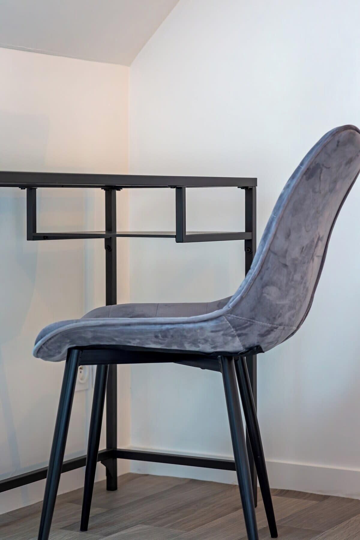 Une chaise dotée d’un haut dossier et d’une structure en métal, placée dans une pièce dont les murs sont blancs et le sol est recouvert de parquet.