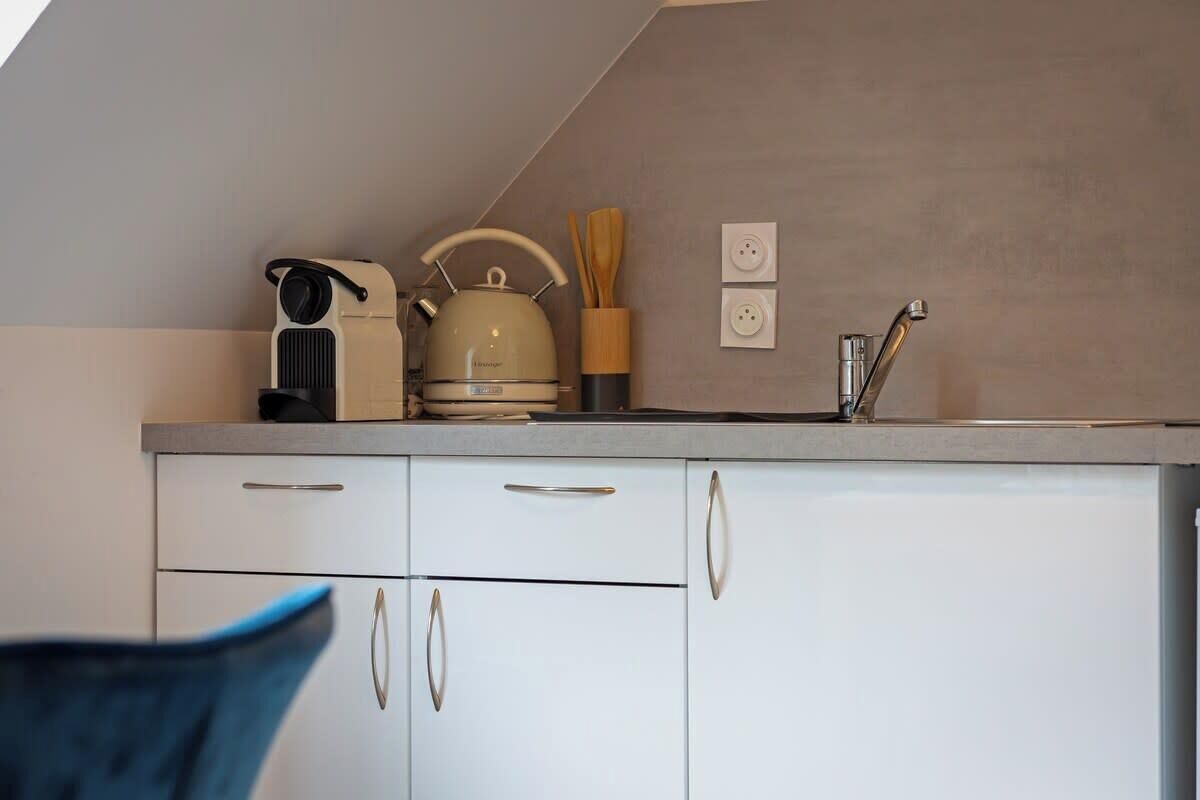 Una kitchenette con hervidor, tostadora y pileta. Hay dos enchufes en la pared y un organizador de utensilios de madera.