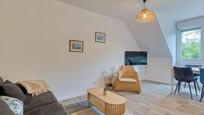 A modern living room with a sofa, a coffee table, a wicker chair, and a dining area with chairs. - Solent, joli F2 proche Jardin des Plantes à Rouen (Rouen)