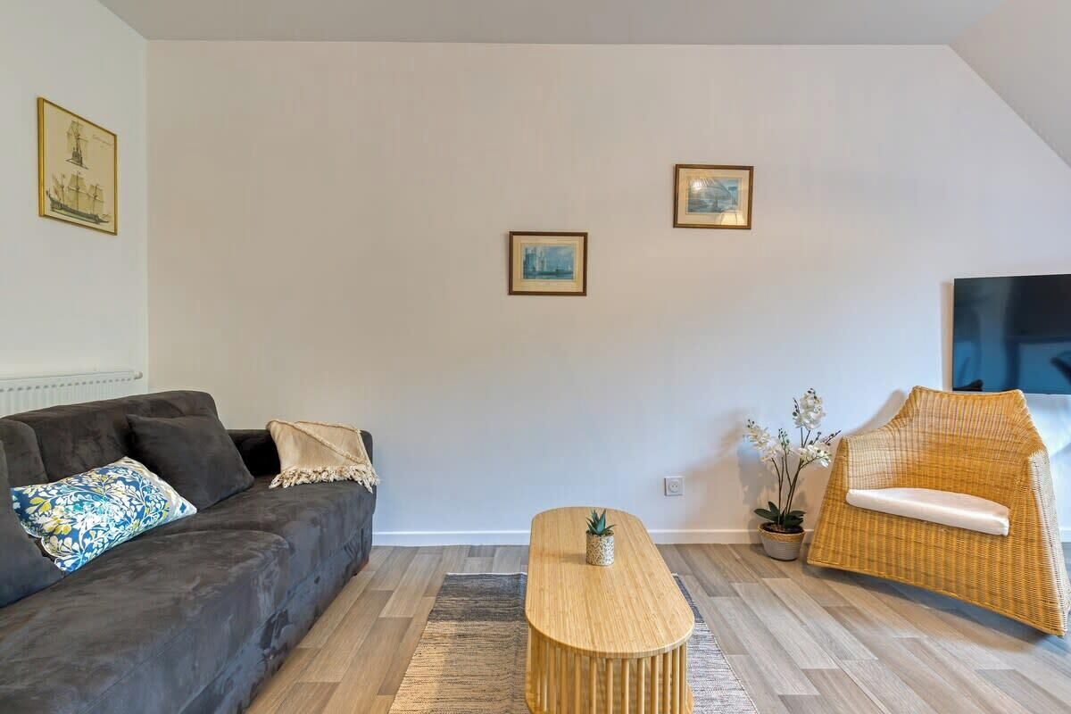 A modern living room with a dark sofa, a wooden coffee table, a wicker chair, and two framed pictures on the wall.